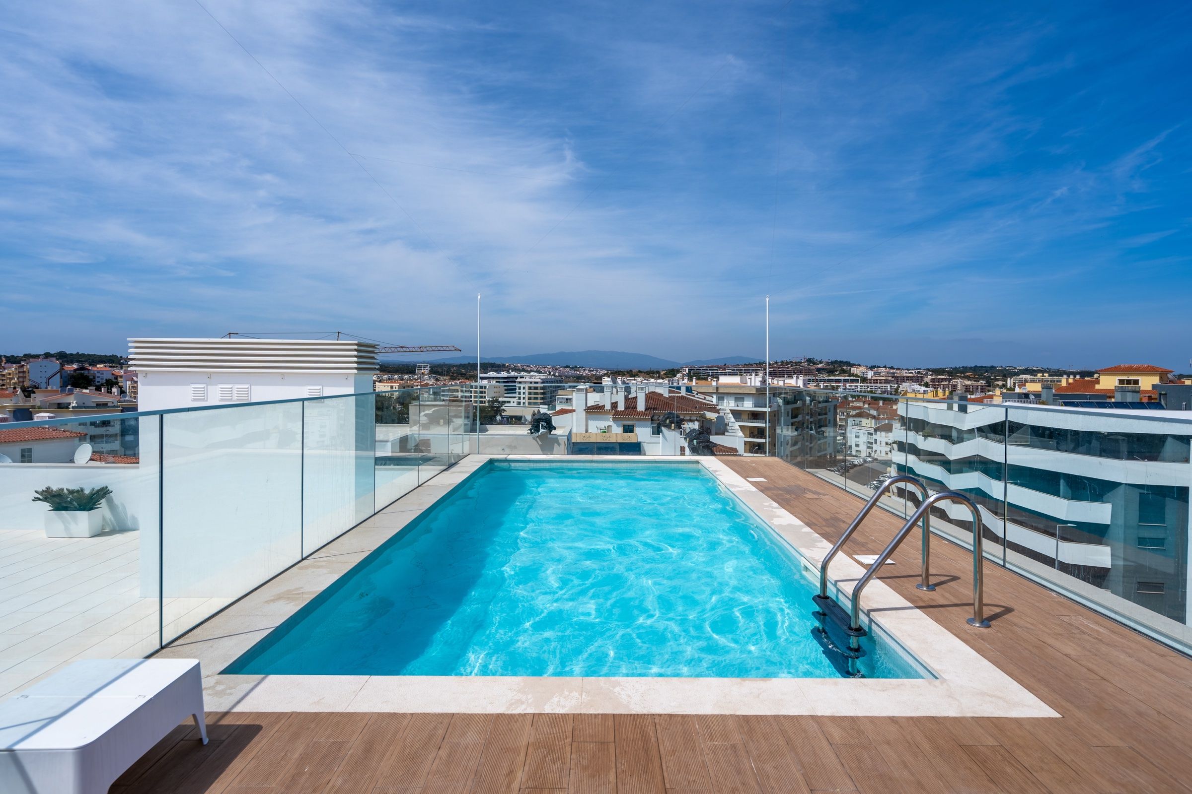 Piscina na cobertura de um prédio moderno, com guarda de vidro e vista sobre a cidade