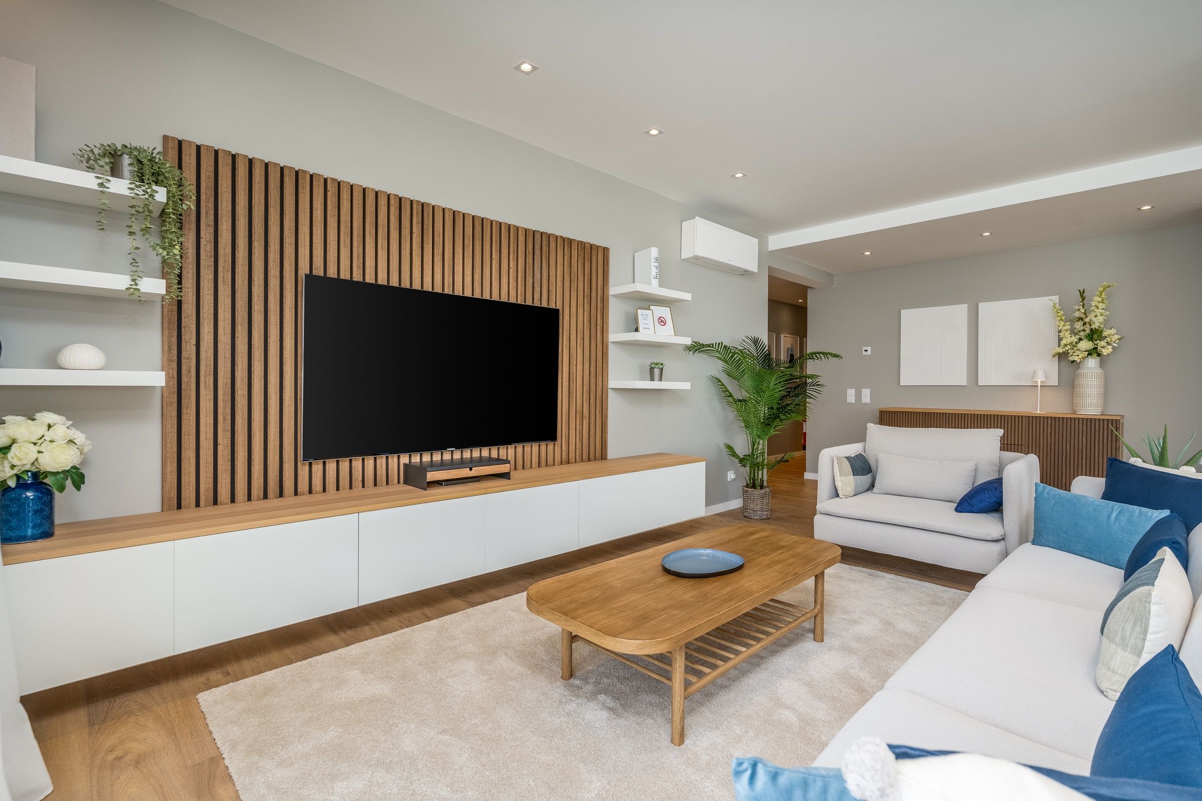 Sala moderna com painel de ripas de madeira, sofás brancos com almofadas azuis e mesa de centro em madeira
