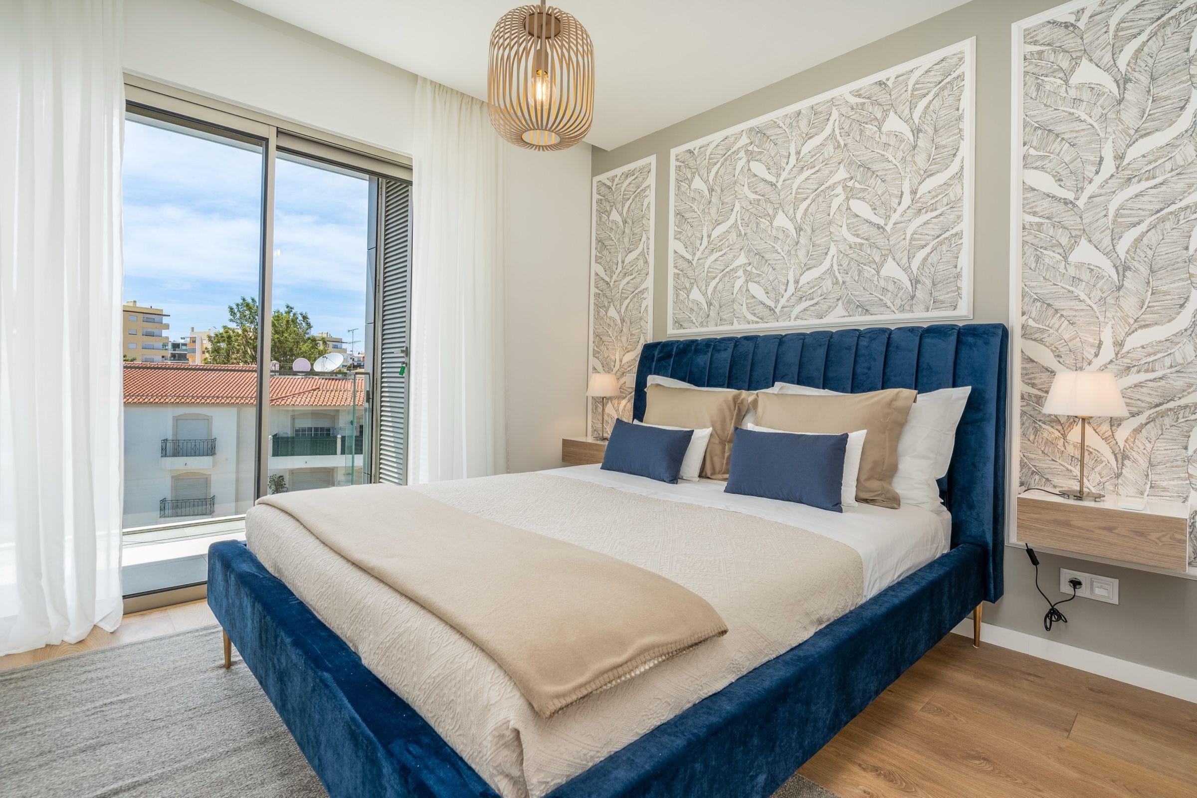 Quarto com cama de veludo azul, papel de parede com folhas e janela de sacada