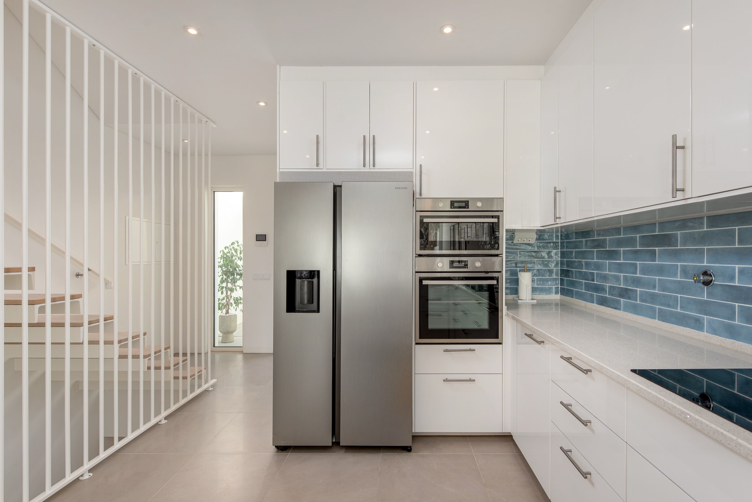 Cozinha branca com azulejo azul, frigorífico americano e escada com guarda de ripas brancas