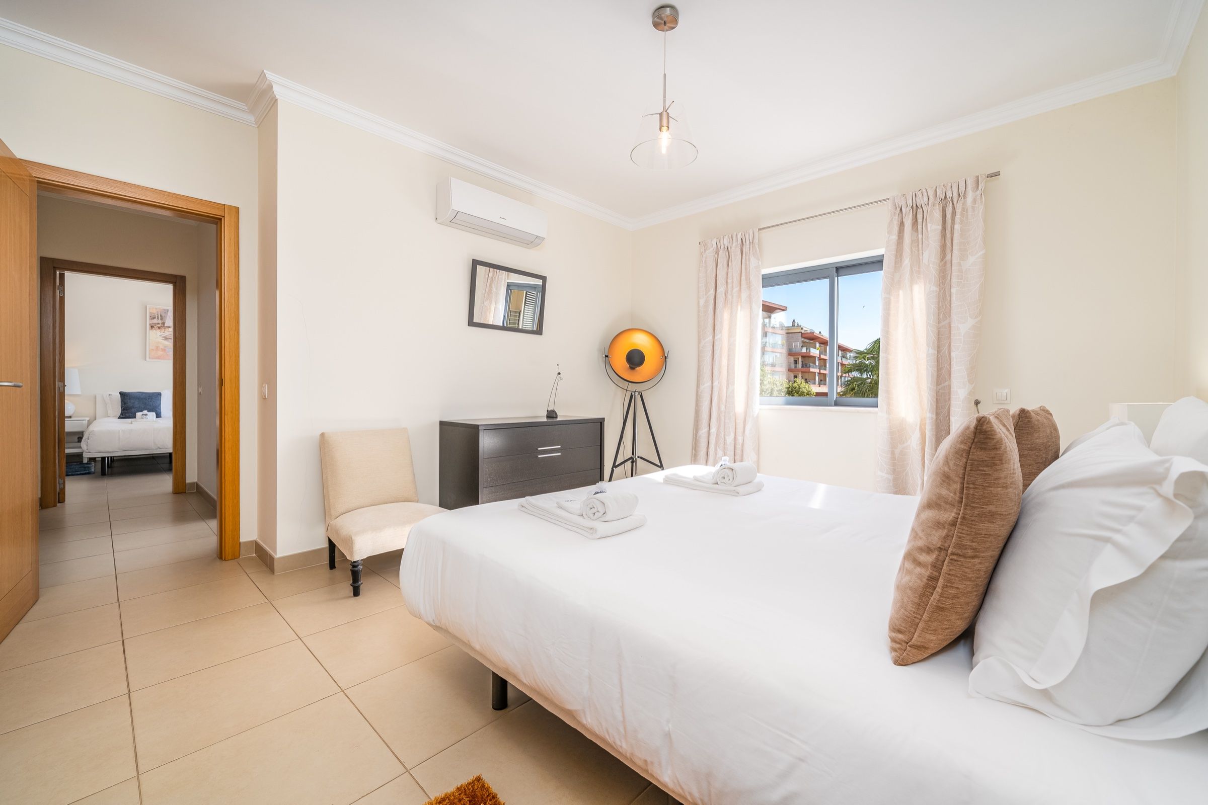 Quarto de casal claro com almofadas castanhas e candeeiro de pé